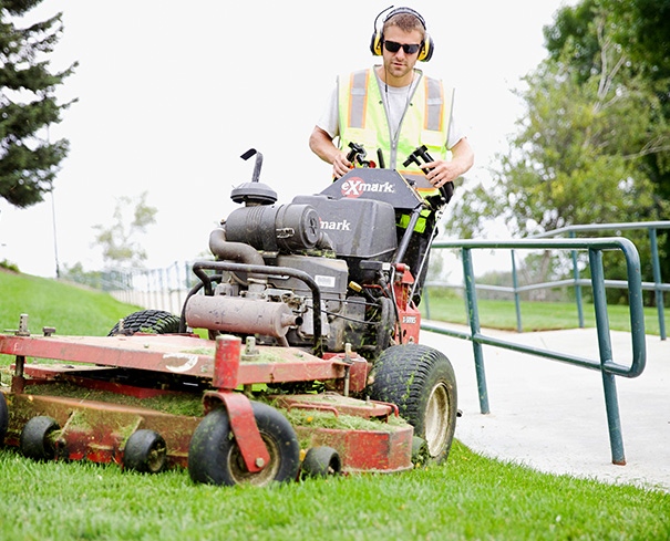 DJ's Landscape Management employee standing on a riding lawn mower to provide landscape maintenance services