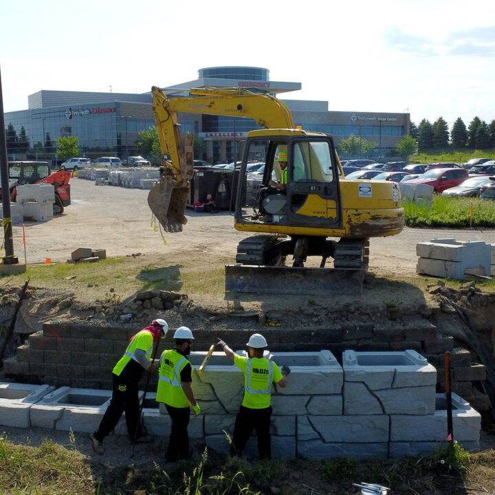 three DJ's employees in yellow safety vests installing a retaining wall while another DJ's employee is operating equipment in the background at a healthcare facility