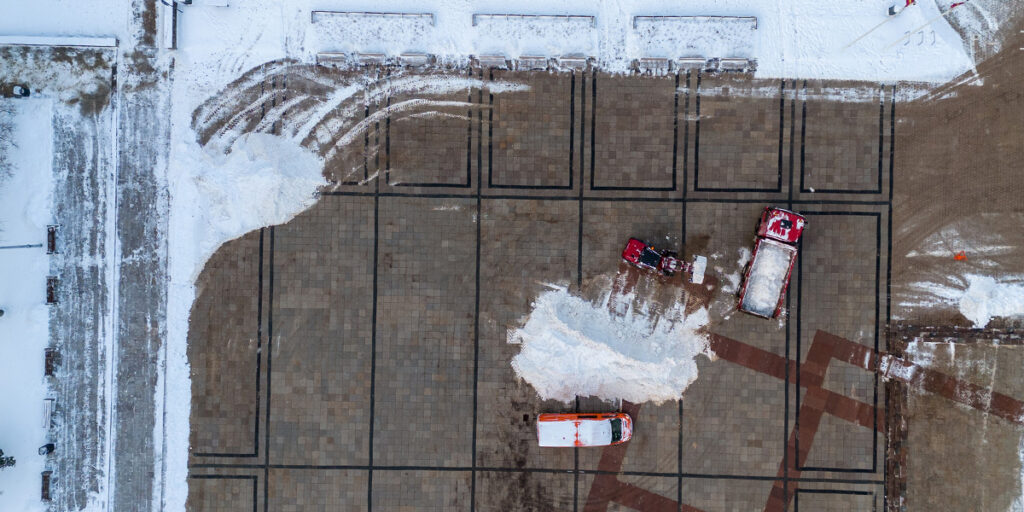 aerial shot of red trucks plowing snow in a parking lot