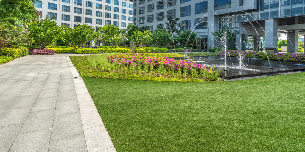 a bright green landscape with a water fountain and pink flowers at a commercial property