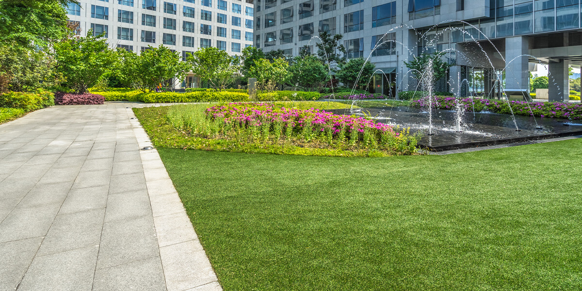 a bright green landscape with a water fountain and pink flowers at a commercial property