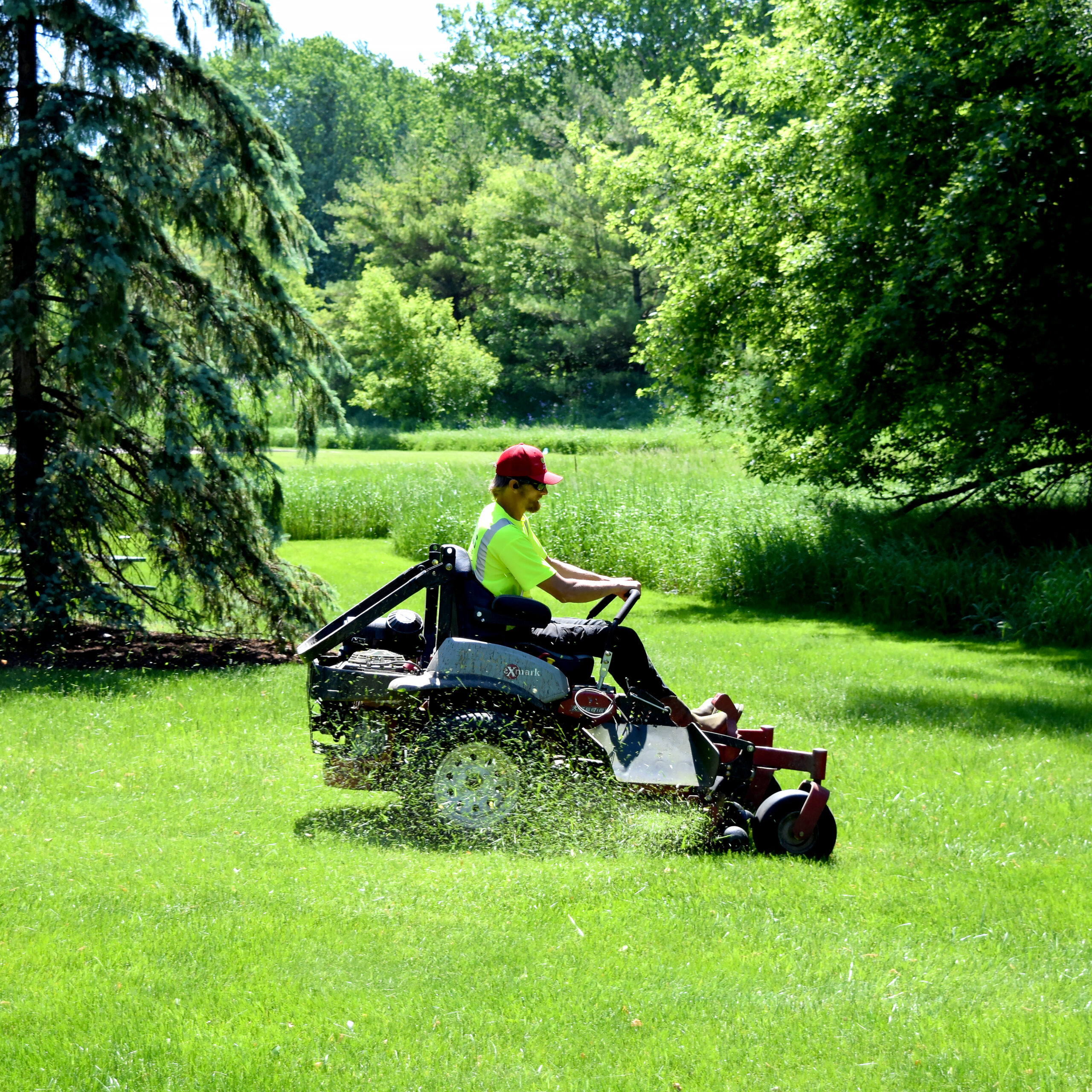 DJ's Landscape Management employee riding a lawn mower cutting grass at a commercial site
